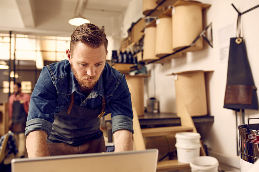 Handsome young business owner with a subtle hipster style working seriously on a lsptop with his bright and neat modern work space behind him